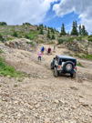 A 4-wheel vehicle below a steep climb, people inspecting above it