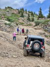 A 4-wheel vehicle below a steep climb, people inspecting above it