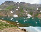 A mountain lake reflecting show patches with a road climbing over a pass above it