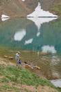 A man, boy and dog on the side of a lake with a snow patch on the other side