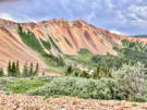 A ridge of red stone and rock slides with rich mountain vegetation below