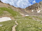 Trail winding across a meadow and then up the steep side of a ridge to a pass