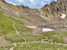 Trail winding across a meadow and then up the steep side of a ridge to a pass