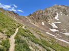 Trail winding across a meadow and then up the steep side of a ridge to a pass