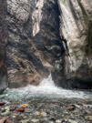 End of a waterfall in a box canyon with colorful rocks in a shallow stream bank