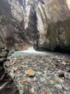 End of a waterfall in a box canyon with colorful rocks in a shallow stream bank