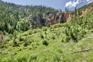A stream falls over bare reddish rock surrounded by mountain greenery