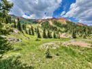 View across a meadow and then trees with a red mountain above