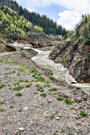 A stream/snow protection barrier over a highway with the stream continuing under a snow bank