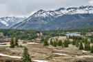 Snow covered peaks and ridge in the background, lake, grassy areas and trees in front
