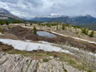 Snow covered ridge in the backgorund, small lake, snow ridges and rock outcrop in the front