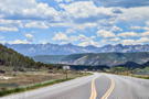 Road curves into a valley surrounded by flat hills; mountains in the distance