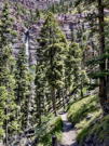 A trail on the side of a mountain slope looking back at a tall waterfall