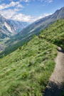 Lone hiker on the trail following a steep grassy mountain slope